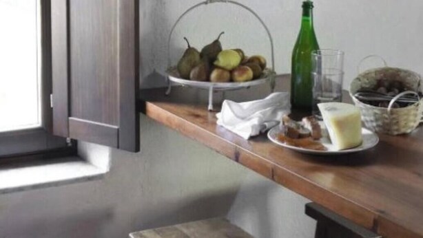 Eine Küche mit einem Holztisch, einer Obstschale, einer grünen Flasche und einem Fenster mit einem Holzjalousie.