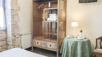 Una habitación con una cama, un armario de madera, una mesa con una lámpara y un televisor en la pared.