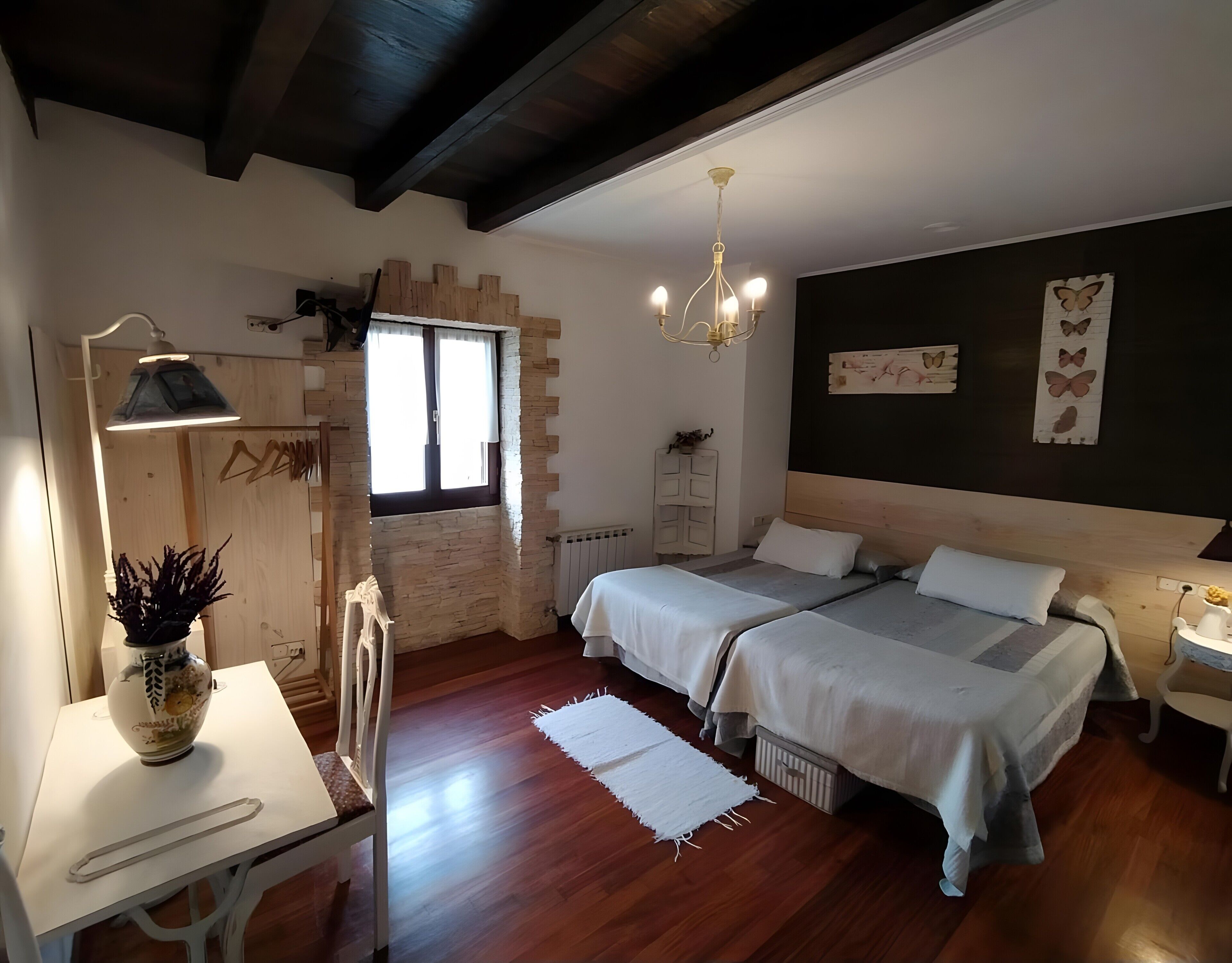 Un dormitorio con dos camas, un candelabro, un ventanal con cortinas, un radiador y una pared decorada con adornos de mariposas.