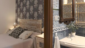 Ein Schlafzimmer mit Bett, Nachttisch, Spiegel und einem Badezimmer inklusive Waschbecken und Spiegel.