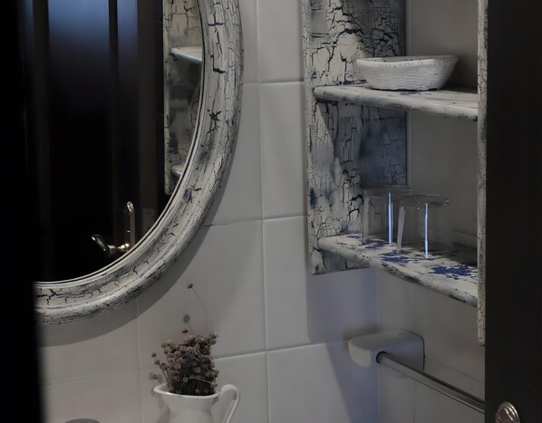 Un baño con pared de azulejos blancos, un lavamanos blanco y un salpicadero similar al mármol, y una jarra blanca con flores secas.