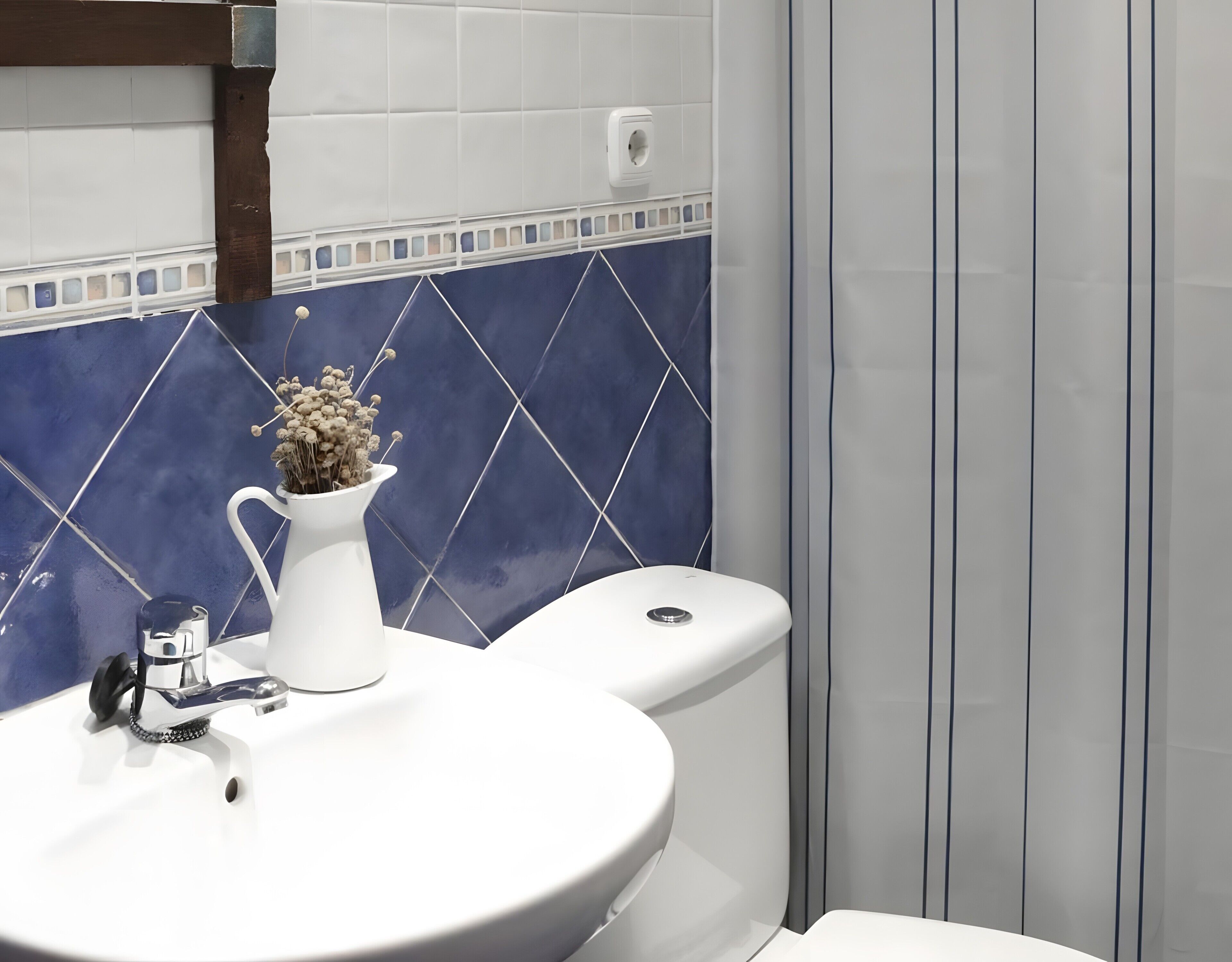 Et badeværelse med en hvid vask, en vase med visne blomster og et toilet.