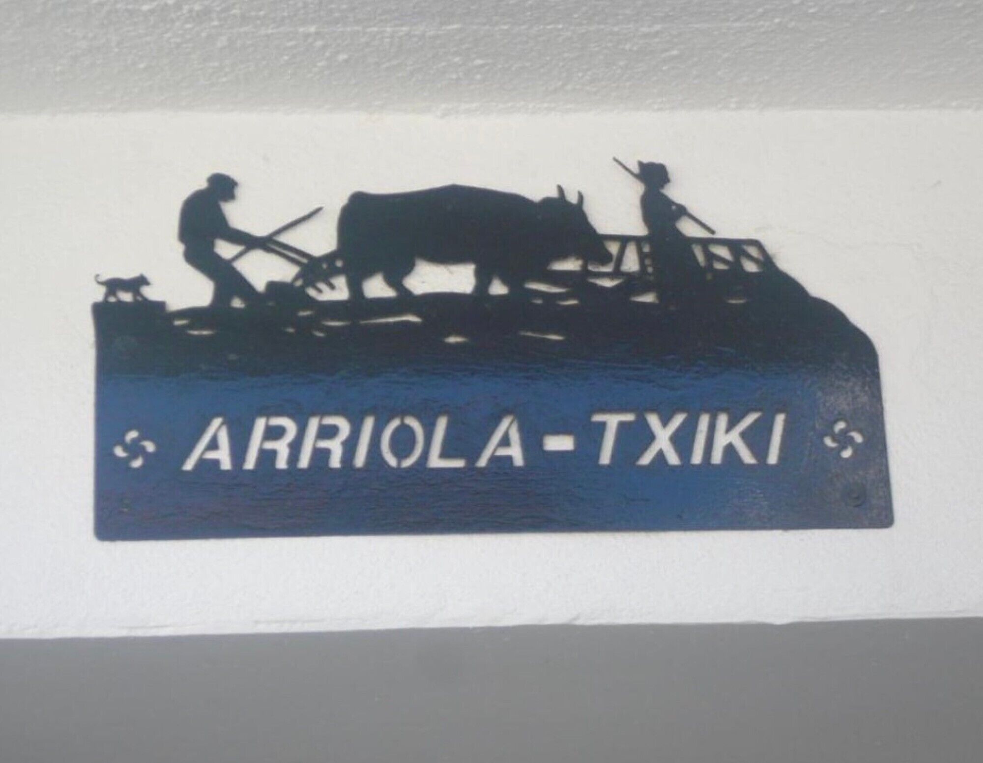 Siluette di una persona con un cane e una mucca su una barca, con il testo 'ARRIOLA-TXIKI'.