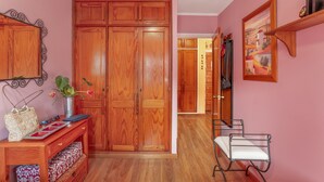 A room with a wooden wardrobe, a bench, a small table with a basket and a plant, and a painting on the wall. - Vacation Home 'Flores with View' with Sea View, Shared Pool and Wi-Fi (Puertorico Mogan)