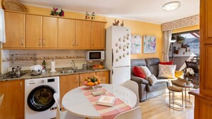 A compact kitchen with wooden cabinets, a washing machine, a microwave, and a refrigerator. - Vacation Home 'Flores with View' with Sea View, Shared Pool and Wi-Fi (Puertorico Mogan)