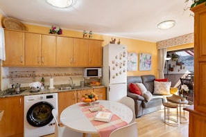 A compact kitchen with wooden cabinets, a washing machine, a microwave, and a refrigerator. - Vacation Home 'Flores with View' with Sea View, Shared Pool and Wi-Fi (Puertorico Mogan)