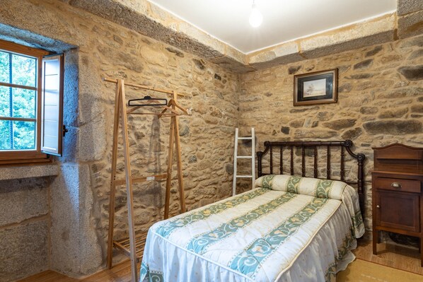 A stone-walled bedroom with a bed, a wooden wardrobe, a hanging rack, and a ladder. - Country House 'Arijón' with Sea View, Private Pool and Wi-Fi (Arteixo)