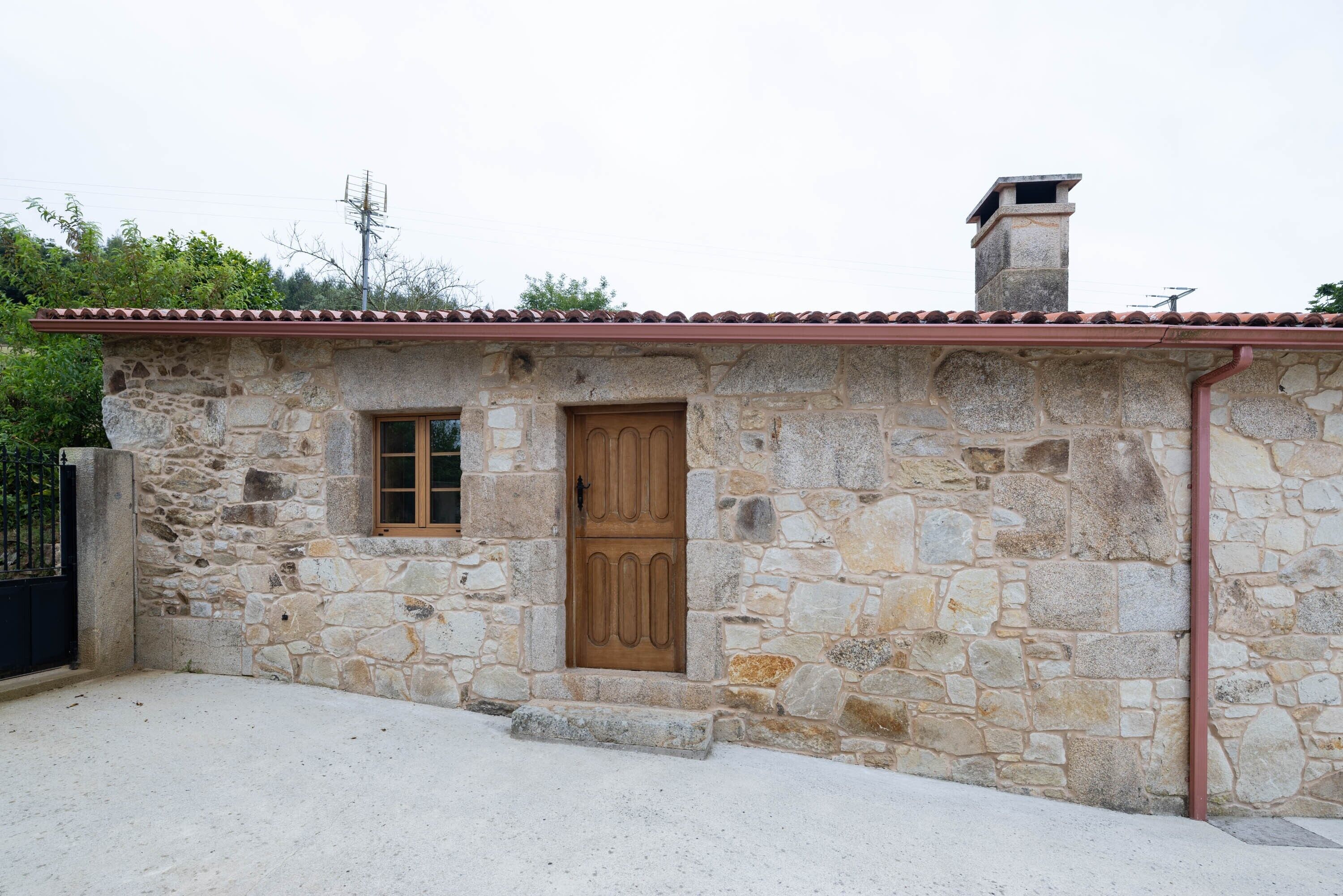 Un edificio de piedra con puerta y ventana de madera, una chimenea y una entrada con portón.