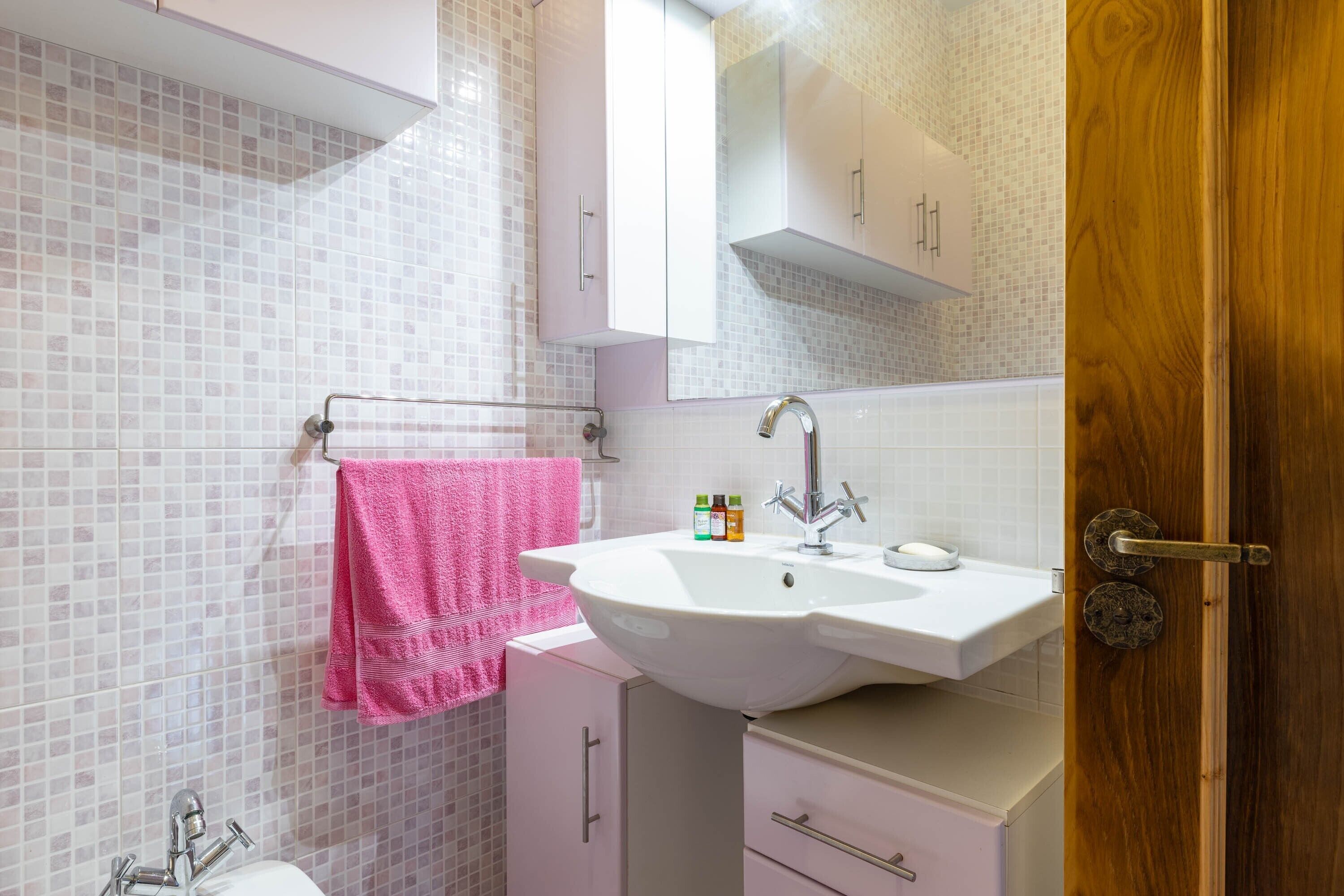 Ein Badezimmer mit einem weißen Waschbecken, einem rosa Handtuch und einer Holztür.