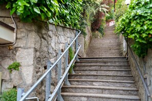 Eine Steintreppe mit Metallgeländern, umgeben von Grünpflanzen und einer Steinmauer.