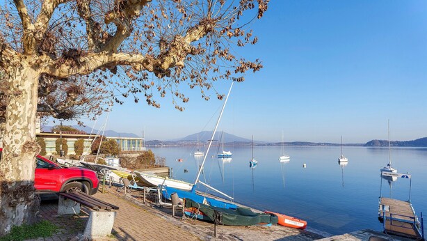 Un muelle sobre el lago con barcos, un coche rojo y un árbol.