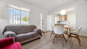Een moderne woonkamer met een bank, eettafel, stoelen, en een keuken die door een open deur zichtbaar is.