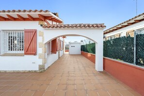 A corridor with a tiled floor, a white building with a red door, and a metal gate.