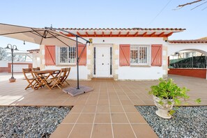 A house with a tiled patio, a dining table with chairs, a potted plant, and a white door.