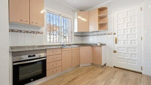 Een keuken met houten kasten, een ingebouwde oven, een raam met metalen tralies en een witte deur met een geometrisch patroon.
