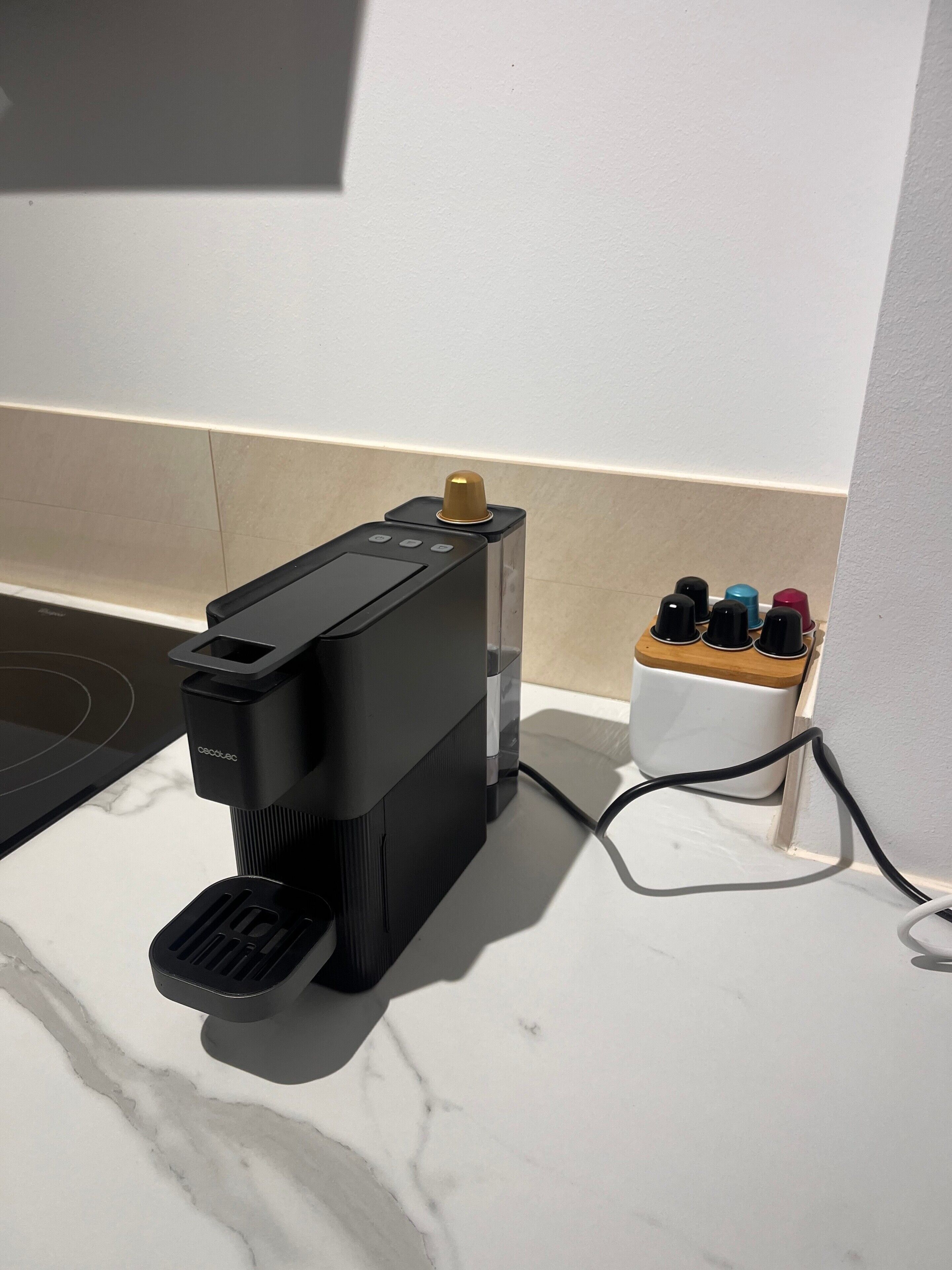 En kaffebryggare står på en bänkskiva, bredvid en grenuttag och en mugghållare med pennor i.