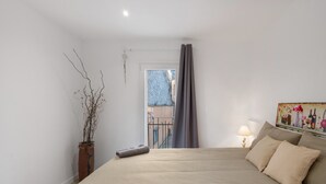Een slaapkamer met een bed, een potplant, een schilderij en uitzicht op buiten.