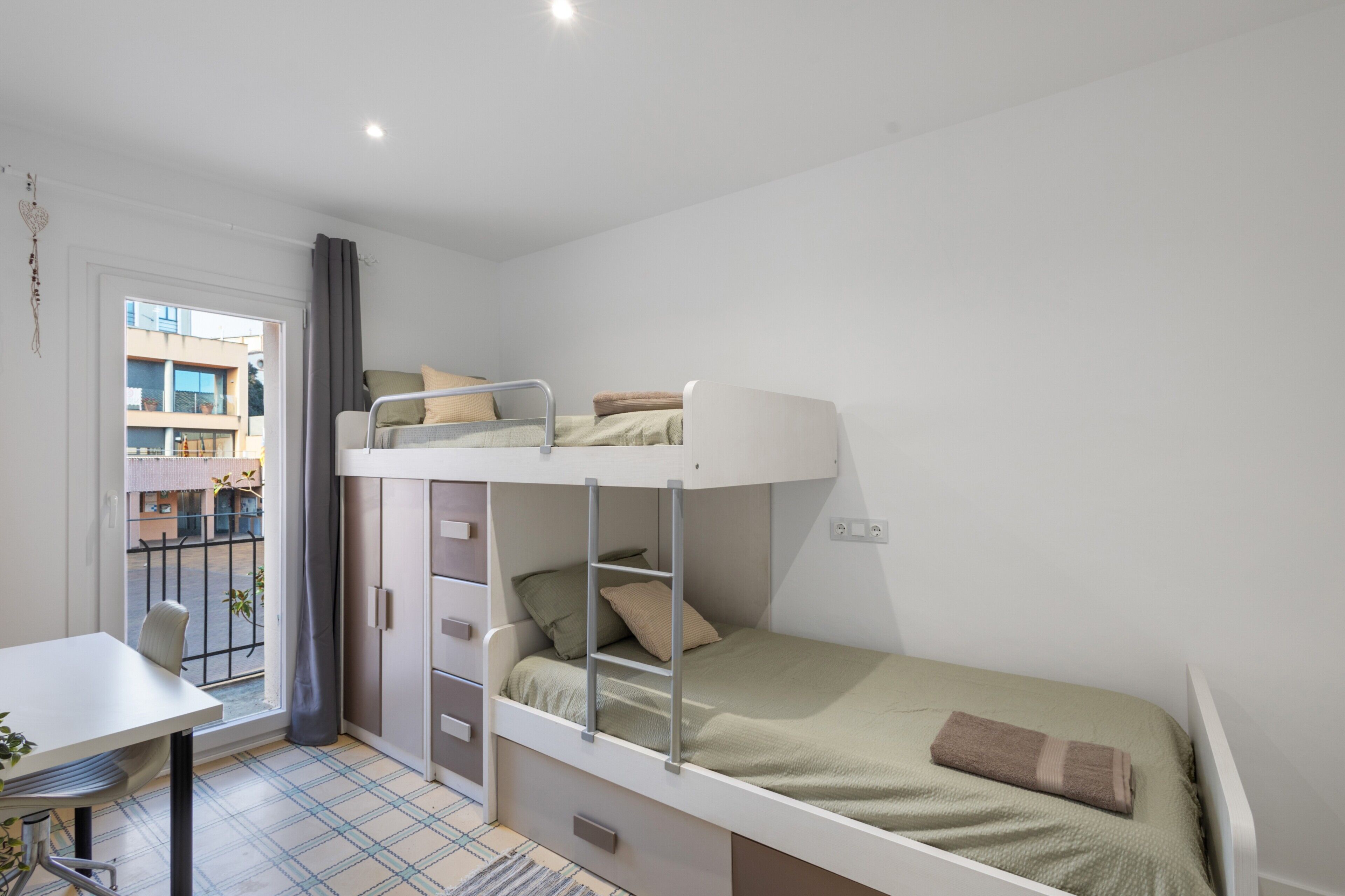 Camera in stile dormitorio con letti a castello, una scrivania e una finestra con vista sugli edifici.