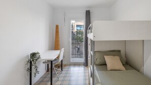 Een kleine, goed verlichte kamer met een stapelbed, een tafel met een stoel en een potplant.