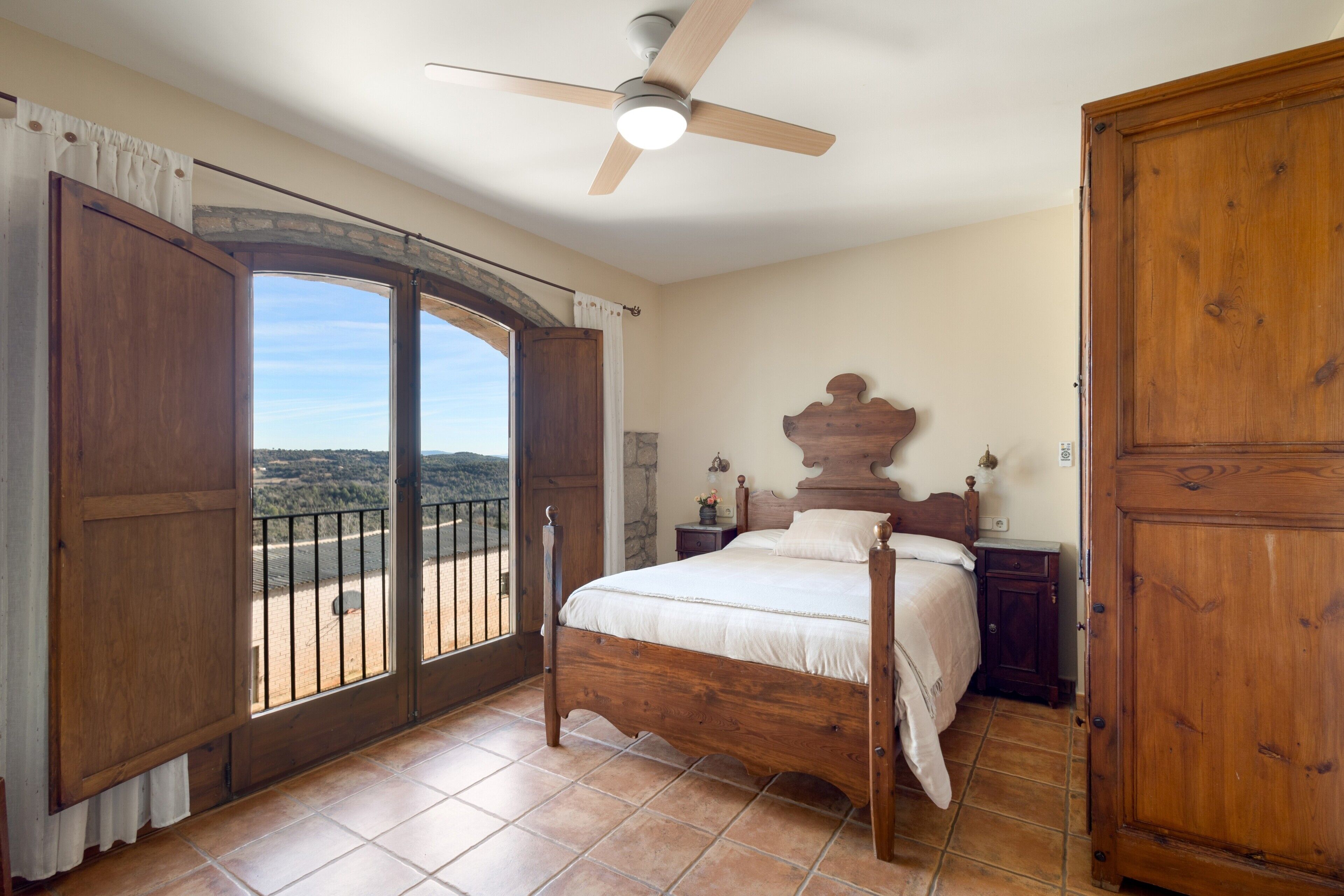 A bedroom with a wooden bed, a nightstand, a dresser, and a balcony with a view.