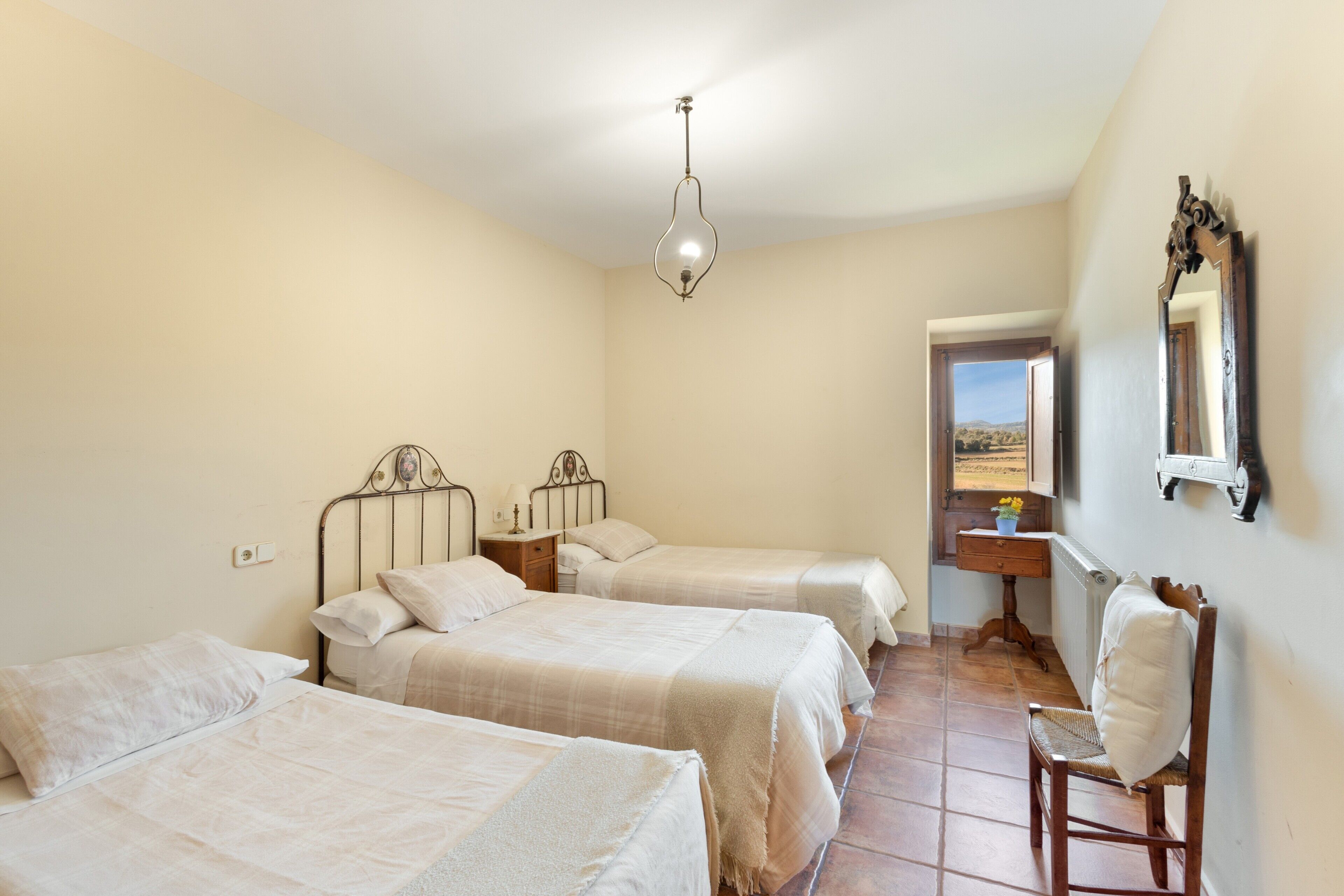 A bedroom with three beds, a chair, a dresser, and a mirror on the wall.