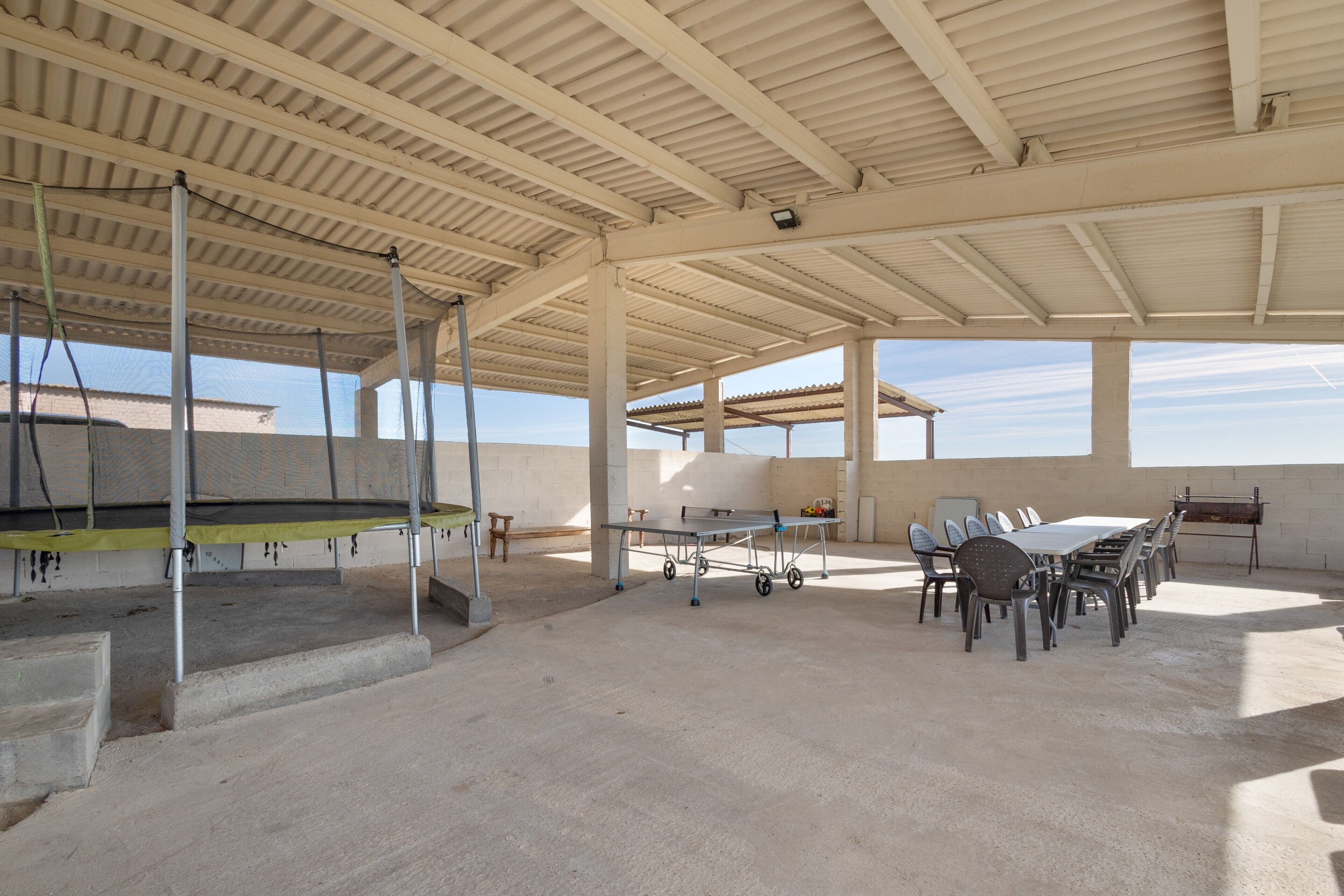 Un patio descubierto y cubierto con mesa de ping pong, sillas y piso de concreto.