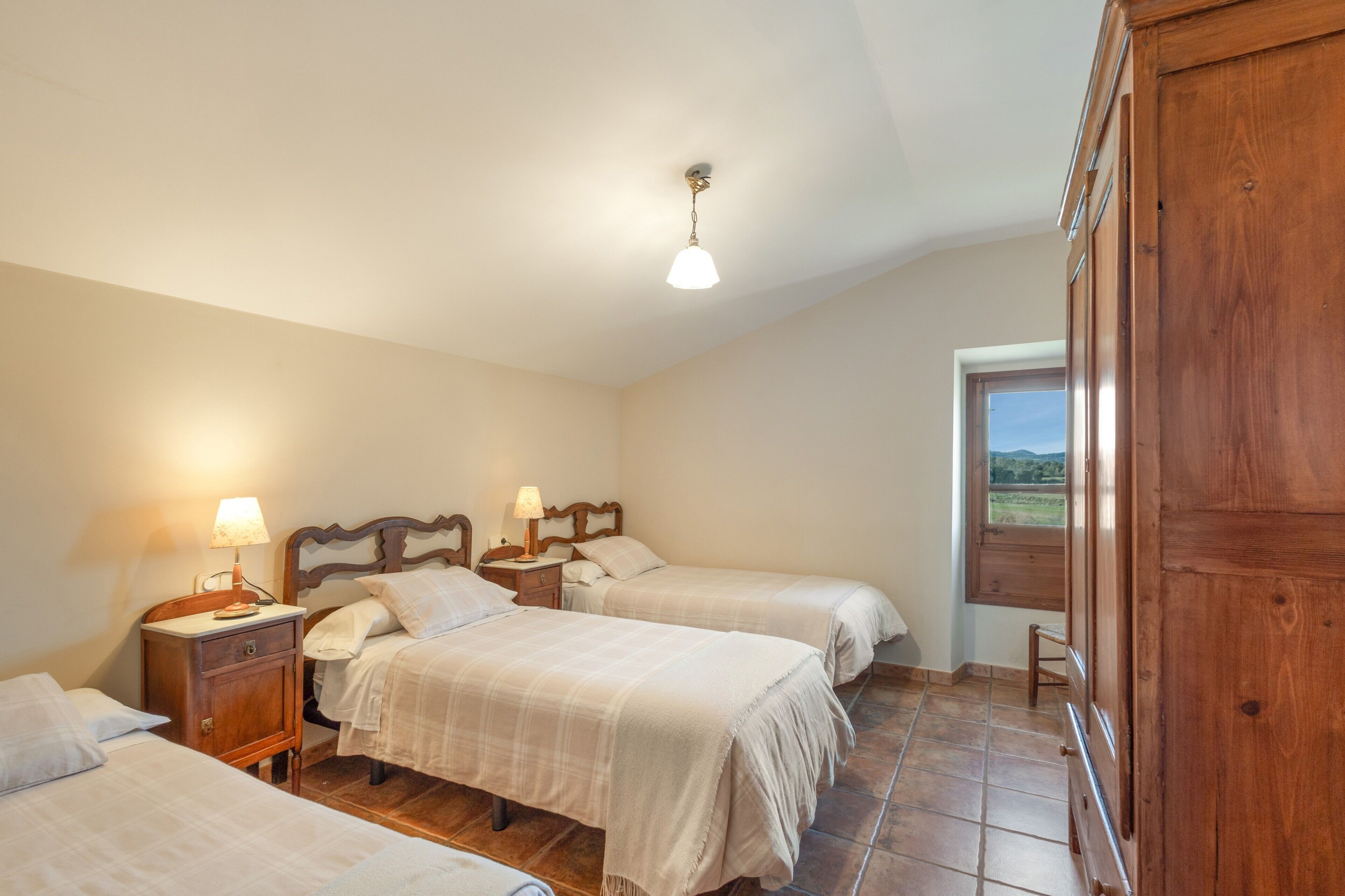Un dormitorio con tres camas, cabeceras de madera, mesitas de noche con lámparas y vistas al exterior a través de una ventana.