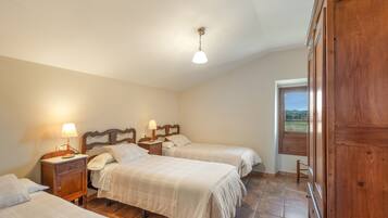 Un dormitorio con tres camas, cabeceras de madera, mesitas de noche con lámparas y vistas al exterior a través de una ventana.