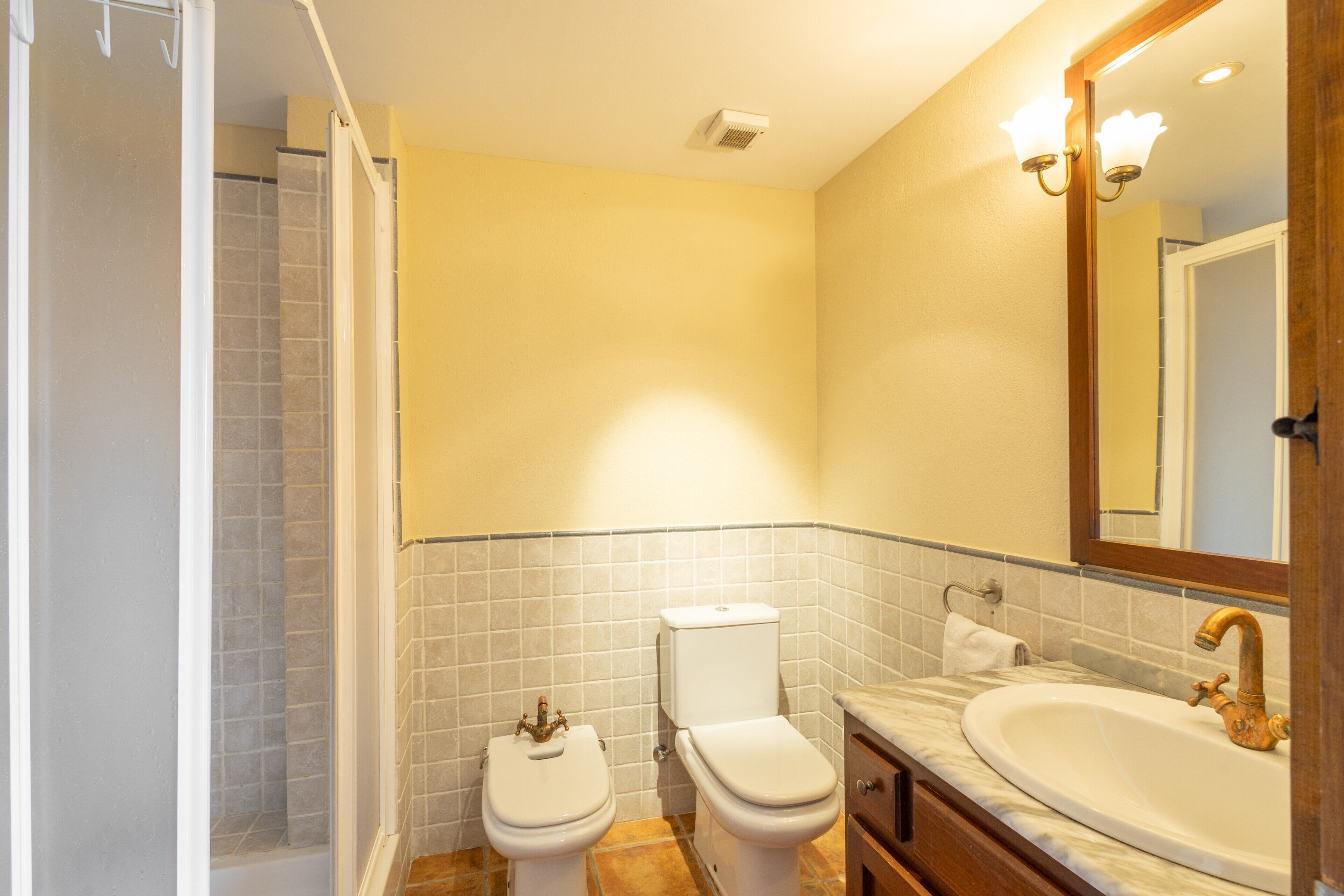 A bathroom with a toilet, sink, mirror, and shower.