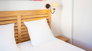 Un letto con testiera in legno, biancheria da letto bianca e una lampada fissata al muro.
