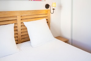 A bed with a wooden headboard, white bedding, and a wall-mounted lamp. - Apartment 'Beg Meil Centre, 300 M De La Plage' with Shared Pool, Shared Garden and Wi-Fi (Fouesnant)