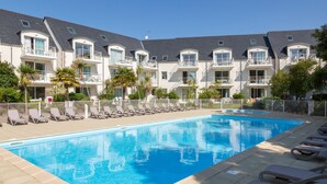 Una piscina con lettini, un edificio con balconi e cielo sereno.