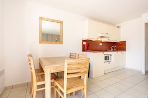 A compact kitchen with a wooden table and chairs, a microwave, and white cabinetry. - Apartment 'Beg Meil Centre, 300 M De La Plage' with Shared Pool, Shared Garden and Wi-Fi (Fouesnant)