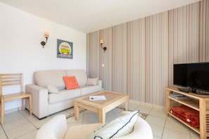 A living room with a sofa, a coffee table, a TV stand, and striped wallpaper. - Apartment 'Beg Meil Centre, 300 M De La Plage' with Shared Pool, Shared Garden and Wi-Fi (Fouesnant)
