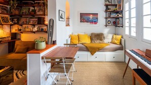 A cozy living room with a sofa, a small table, a keyboard, and a bookshelf filled with books and decorative items. - Cozy renovated studio in central Biarritz - 2 min to beaches & market - Absolute calm (Biarritz)