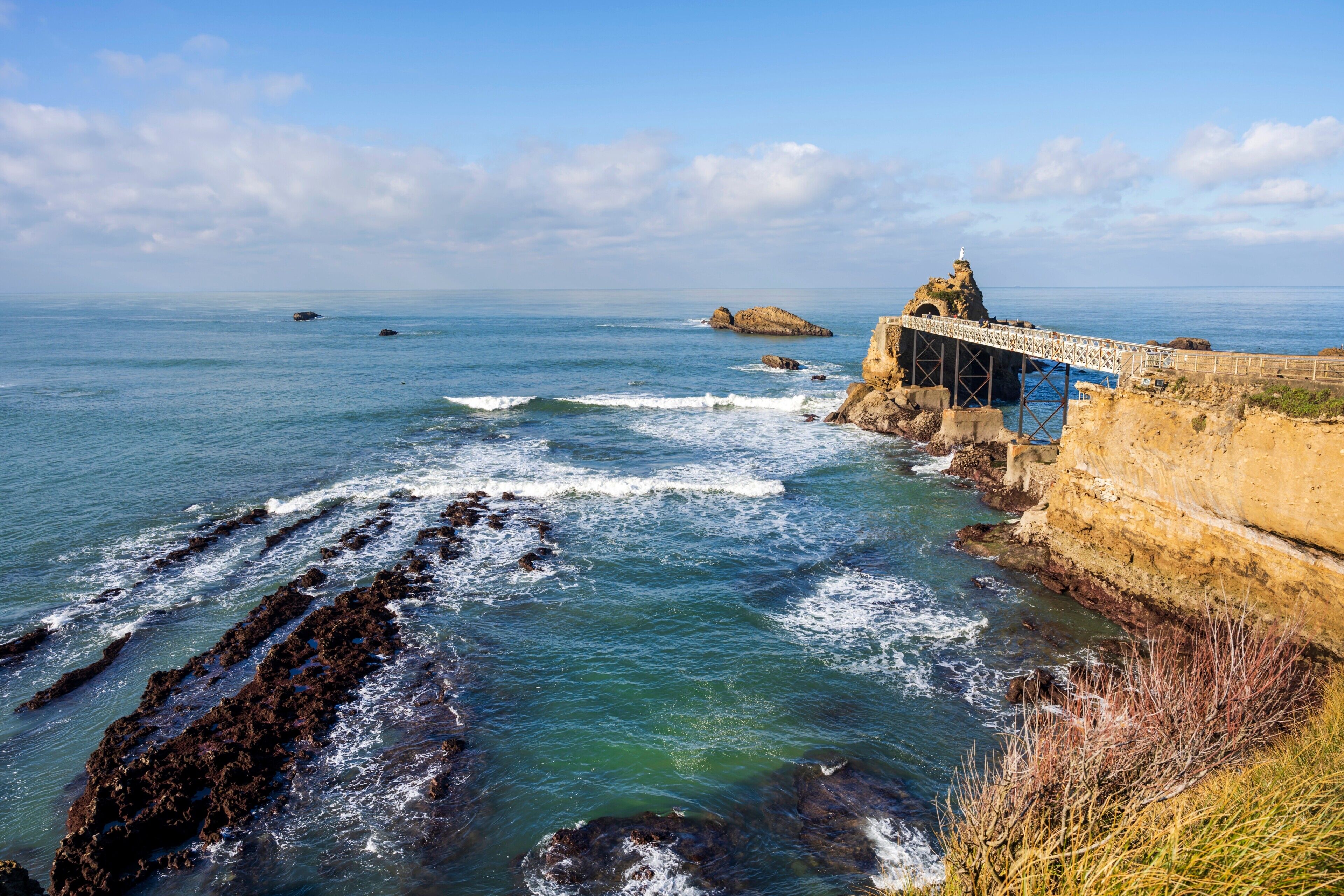 A coastal landscape with a bridge, rocky shoreline, and clear blue sky.