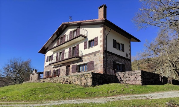 A two-story house with a stone foundation, a balcony on the upper floor, and a chimney. - Country House 'Autxikoborda Bajo' with Mountain View, Private Garden and Wi-Fi (Elizondo)