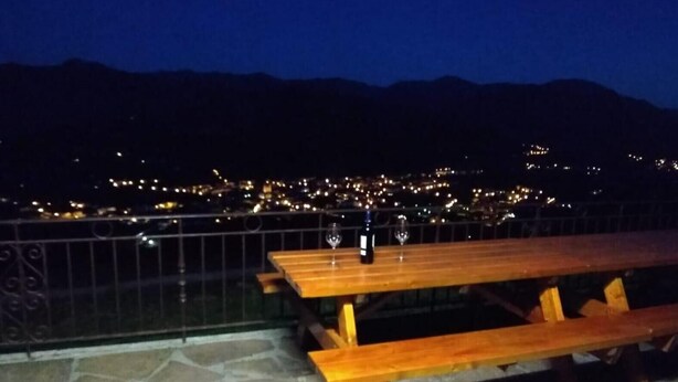 A wooden picnic table with a wine bottle and glass on it, set against a stone-paved patio with a metal railing. - Country House 'Autxikoborda Bajo' with Mountain View, Private Garden and Wi-Fi (Elizondo)