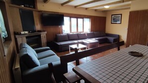 A room with a sofa, a table with a checkered tablecloth, a television mounted on the wall, and wooden paneling. - Country House 'Autxikoborda Bajo' with Mountain View, Private Garden and Wi-Fi (Elizondo)