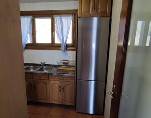 A kitchen with wooden cabinets, a stainless steel refrigerator, a sink, and a window with curtains. - Country House 'Autxikoborda Bajo' with Mountain View, Private Garden and Wi-Fi (Elizondo)
