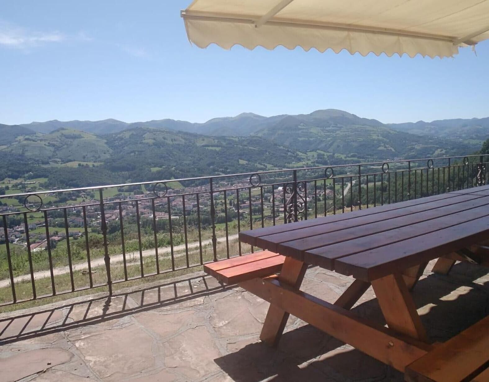 Una mesa y banco de madera en un balcón con vistas a un valle y montañas.