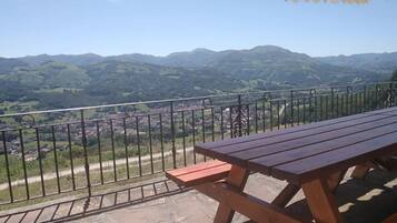 Una mesa y banco de madera en un balcón con vistas a un valle y montañas.