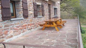 Ein Steinhaus mit Holzläden, einem Picknicktisch und einem Metallgeländer.