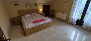 Una camera da letto con un letto, comodini, una sedia, un termosifone e una finestra con tende.
