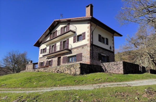 Una casa a due piani con fondamenta in pietra, un balcone al piano superiore e un camino.