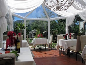 A covered outdoor dining area with tables, chairs, and a chandelier.