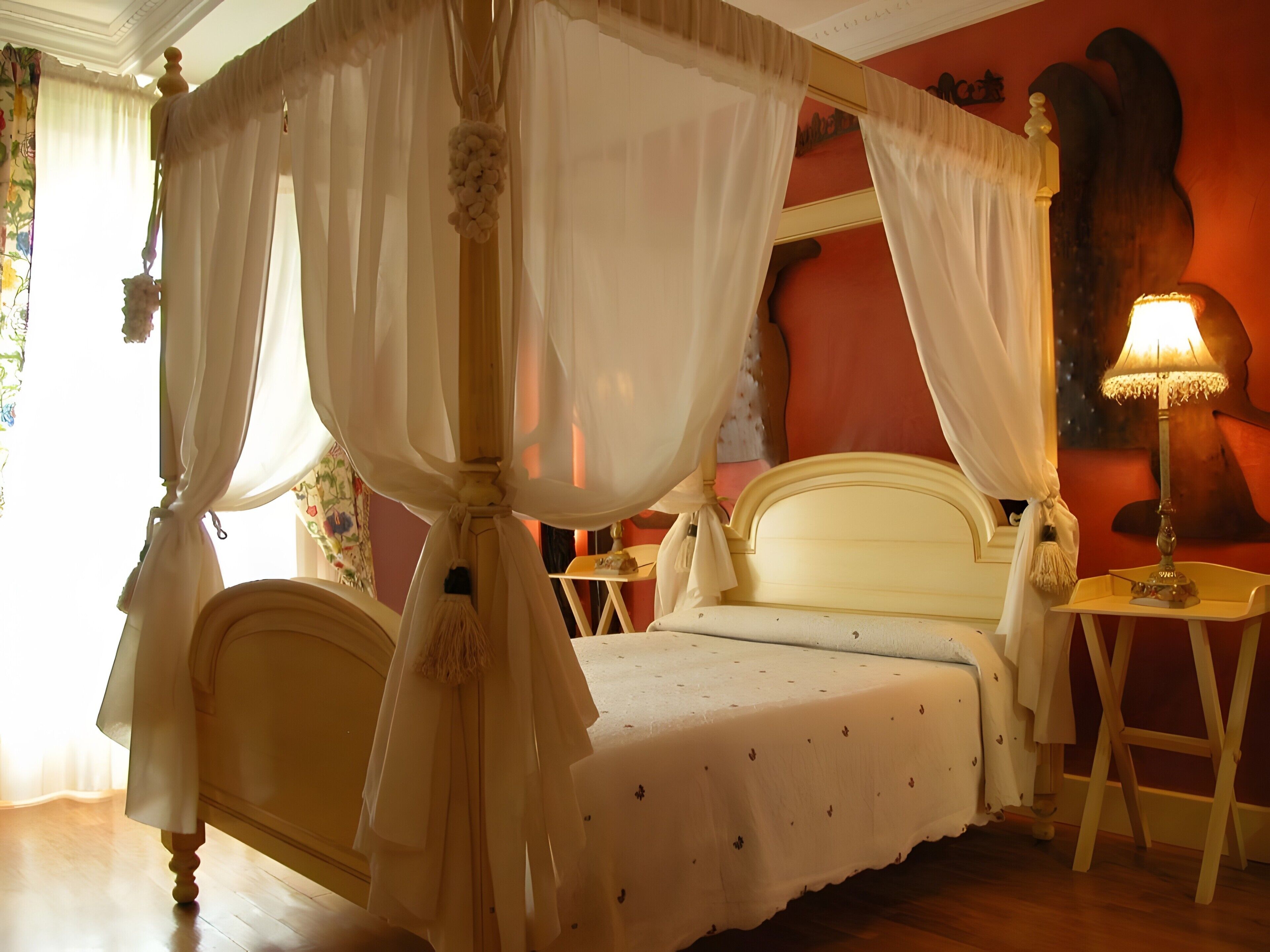 Un lit à baldaquin à quatre poteaux, recouvert d’une courtepointe blanche, une table de chevet avec une lampe et un mur orné d’un tableau.