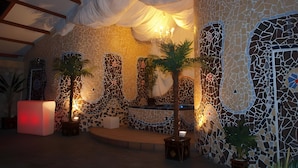 A room with a mosaic wall, a central seating area, and a ceiling with draped fabric.