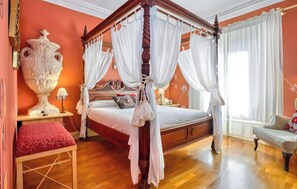 A four-poster bed with white drapes, a large vase, a red bench, and a wooden floor.