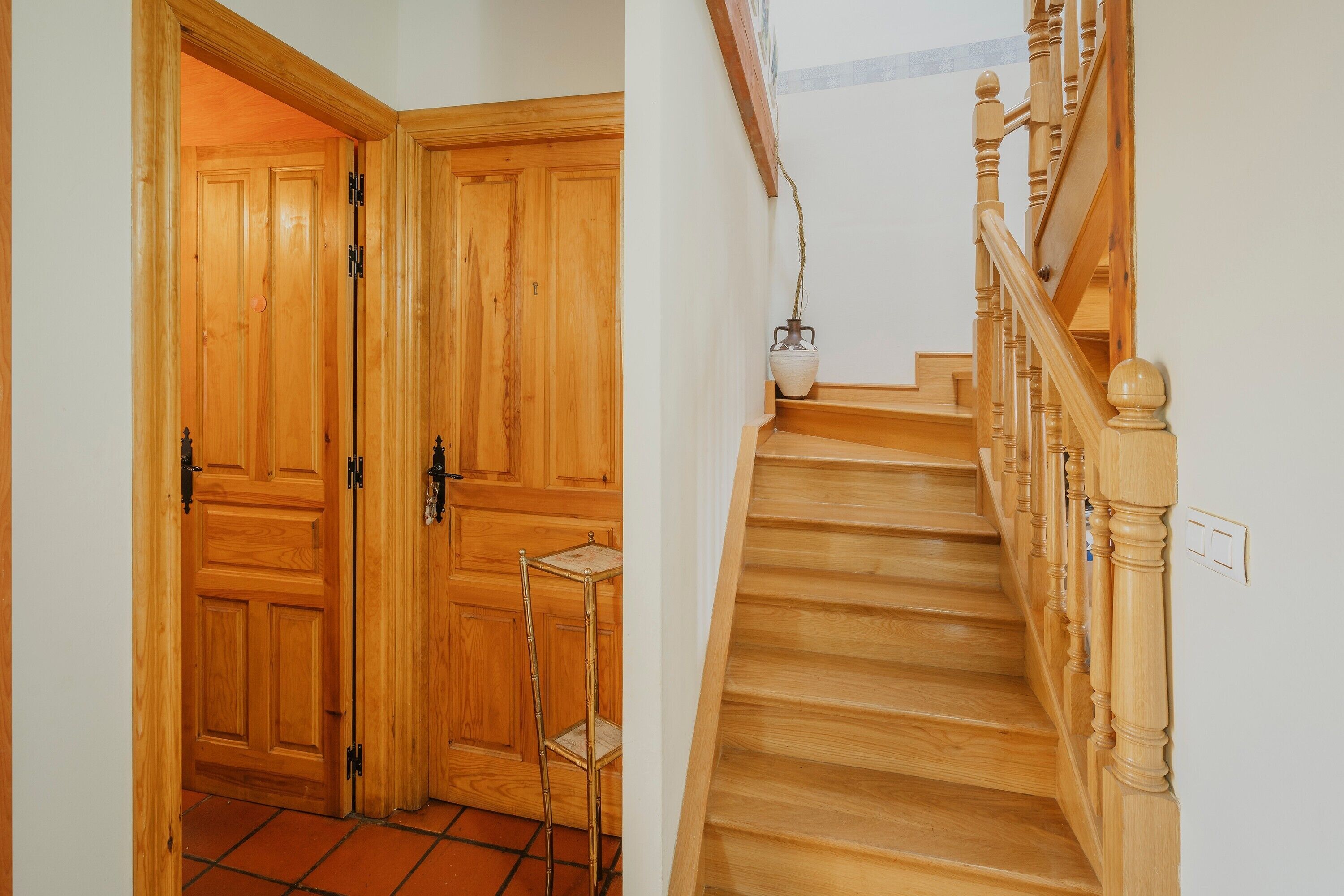 Una escala de fusta amb barana i una porta amb prestatgeria metàl·lica.